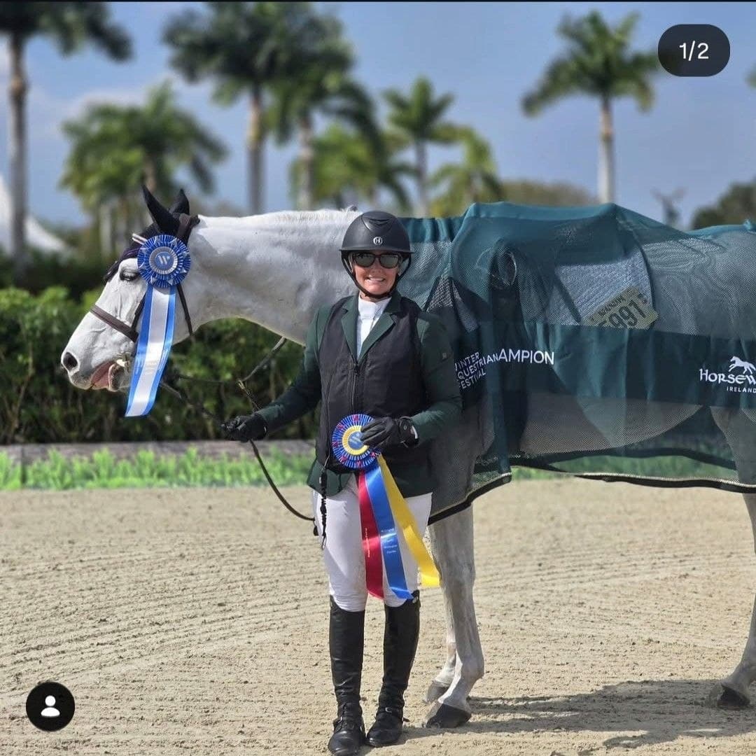 Gray horse and rider posing with championship ribbons at a horse show